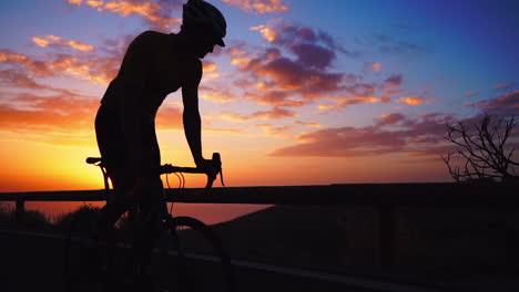 la silueta en cámara lenta revela al atleta en bicicleta en una serpentina de montaña, apreciando la vista de la isla, personificando un compromiso con un estilo de vida saludable al atardecer