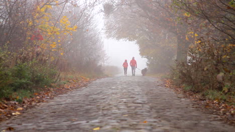 Una-Pareja-Con-Abrigos-Rojos-Está-Paseando-A-Su-Perro-Por-Un-Camino-Pavimentado-De-Piedra-Durante-Una-Mañana-Nublada-Y-Nublada