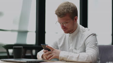 handsome man in white shirt and glasses is using smartphone in cafe or coworking area businessman or freelancer