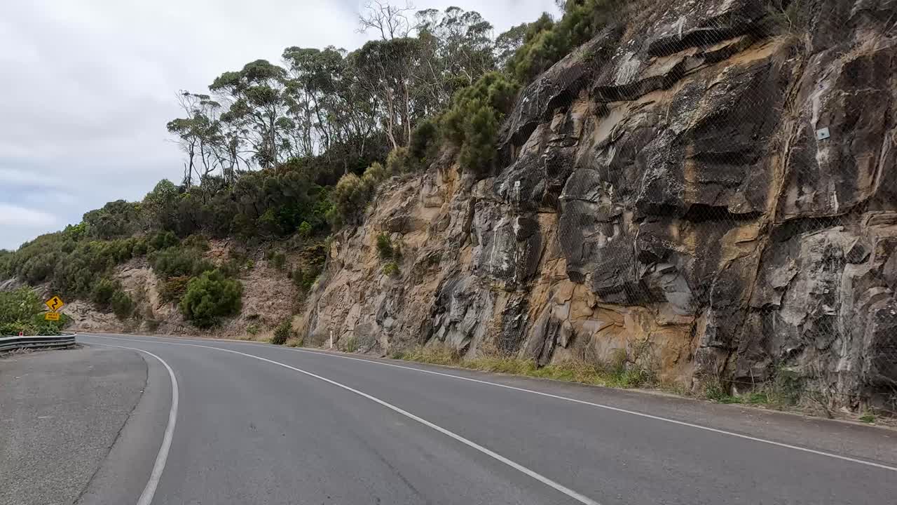 A 14-second video capturing a winding road through lush greenery and rocky cliffs under a cloudy sky