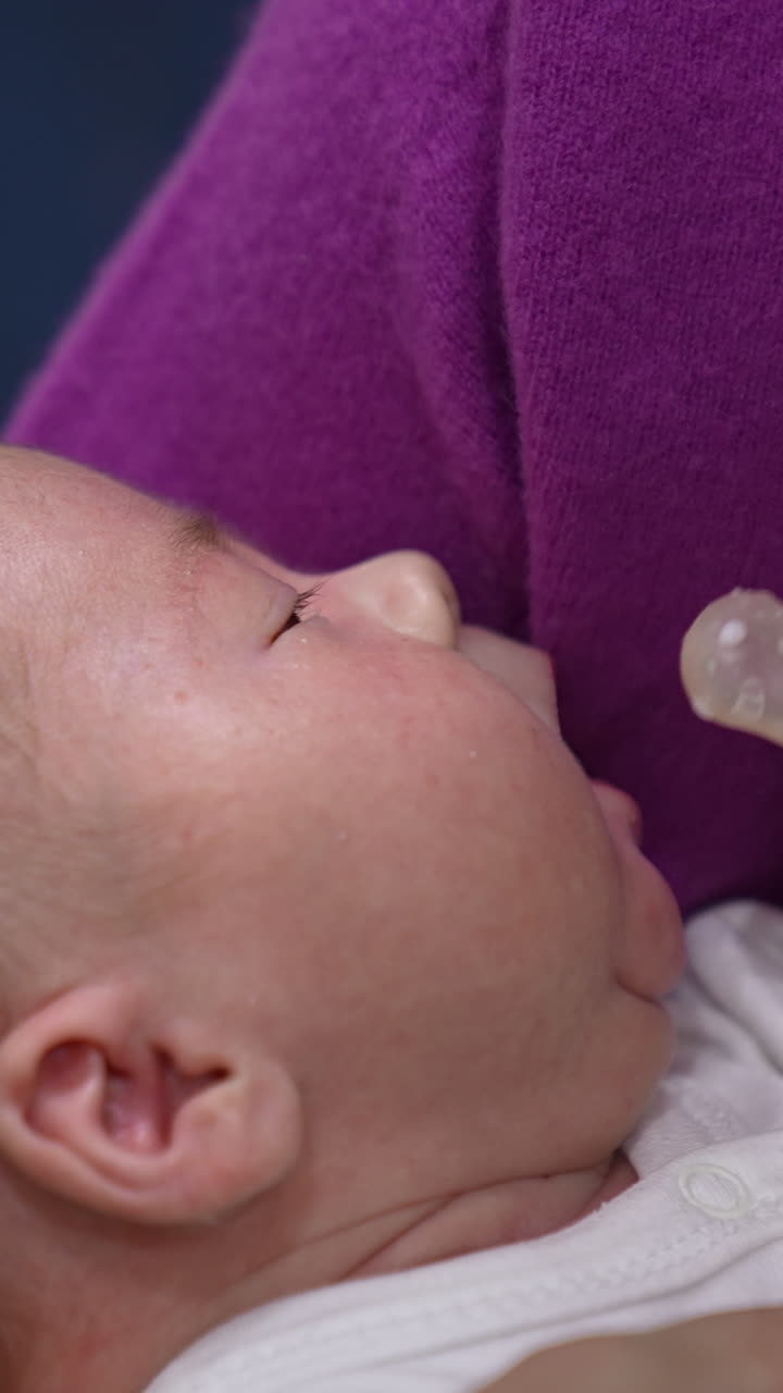 Baby lying in mommy's hands ready to be fed. Baby grasping the pacifier of the bottle and suckling hungrily. Close up. Vertical video