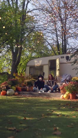 two women relaxing in autumn garden near camper trailer