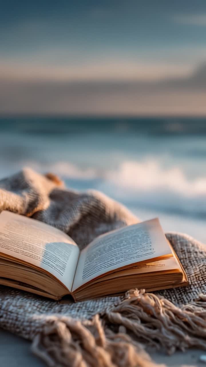 Un libro aperto che riposa su una coperta accogliente sulla tranquilla riva del mare al tramonto, evocando un senso di pace e serenità nell'abbraccio della natura