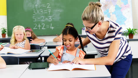 teacher helping schoolgirl with their homework in classroom