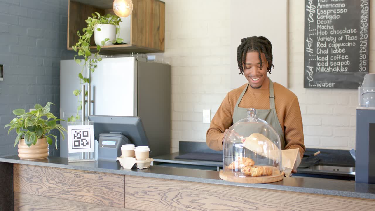 Homem afro-americano de avental na abertura do café, embalando croissant para pedido em um saco, recolocando a cúpula.