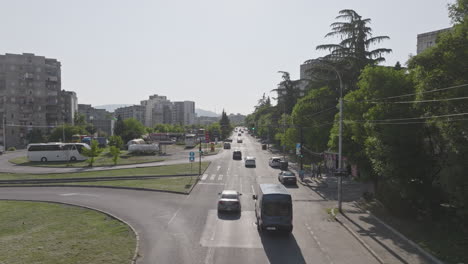 Cinematic-footage-of-cars-drive-at-cross-road-surrounded-by-buildings-and-trees