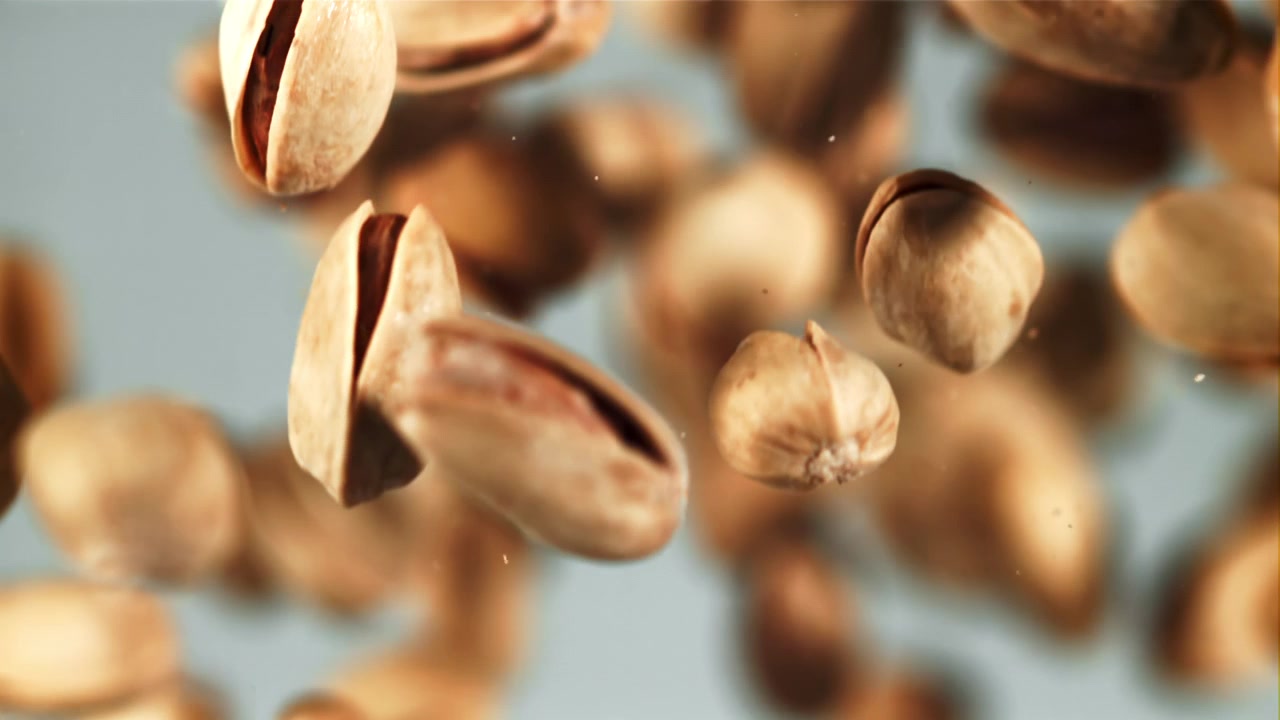 Pistacchi tostati che cadono al rallentatore su uno sfondo chiaro.