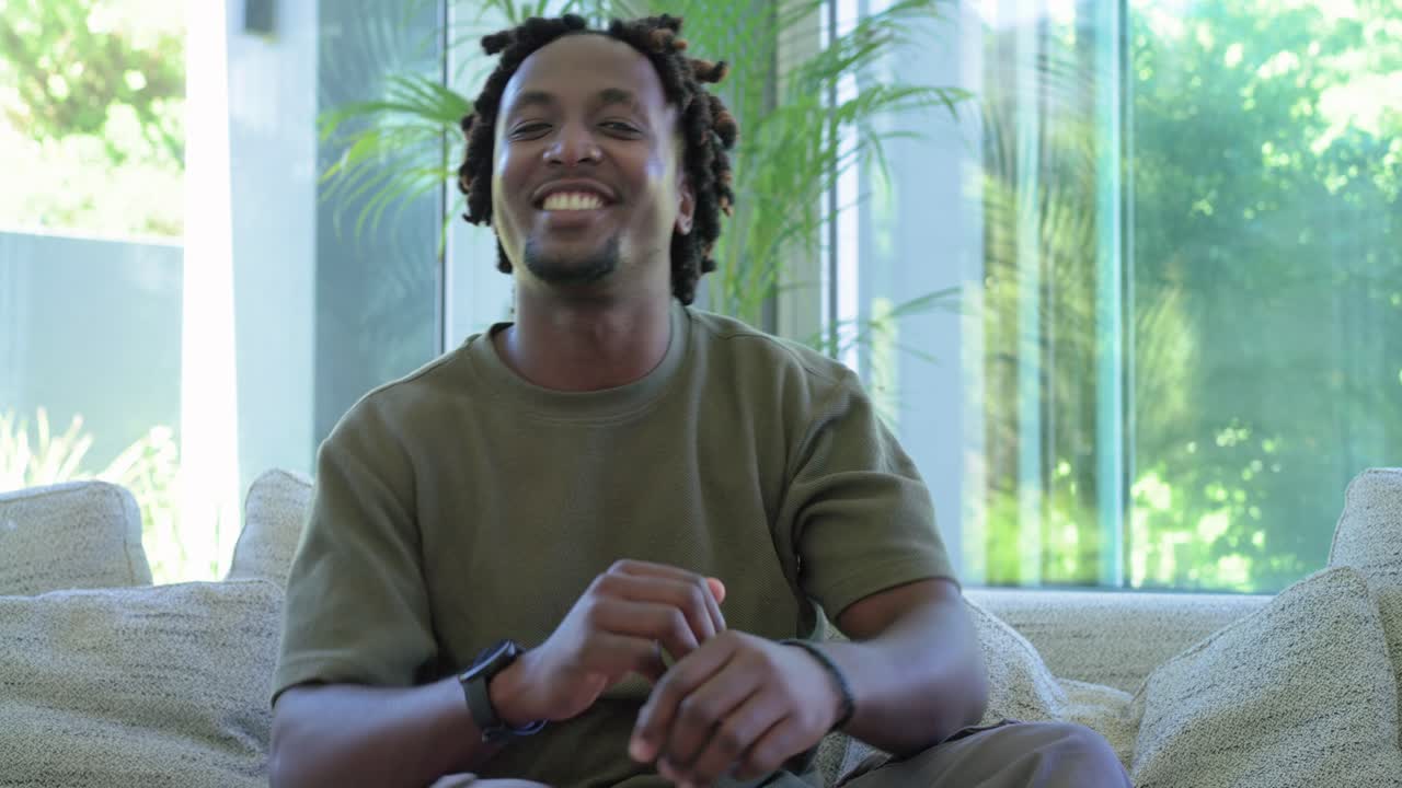 Camera moving in, African American man turning to camera, smiling and laughing on sectional sofa