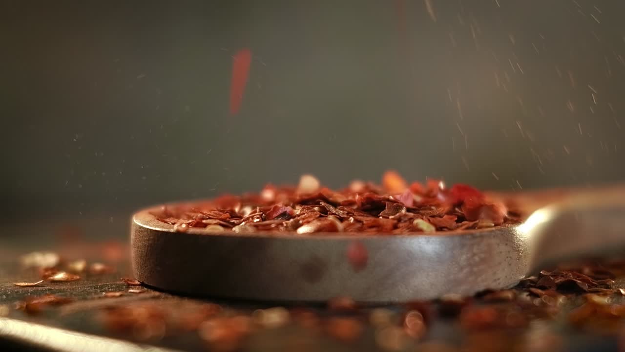 Flakes of red hot chili pepper in wooden spoon closeup on a kitchen table.