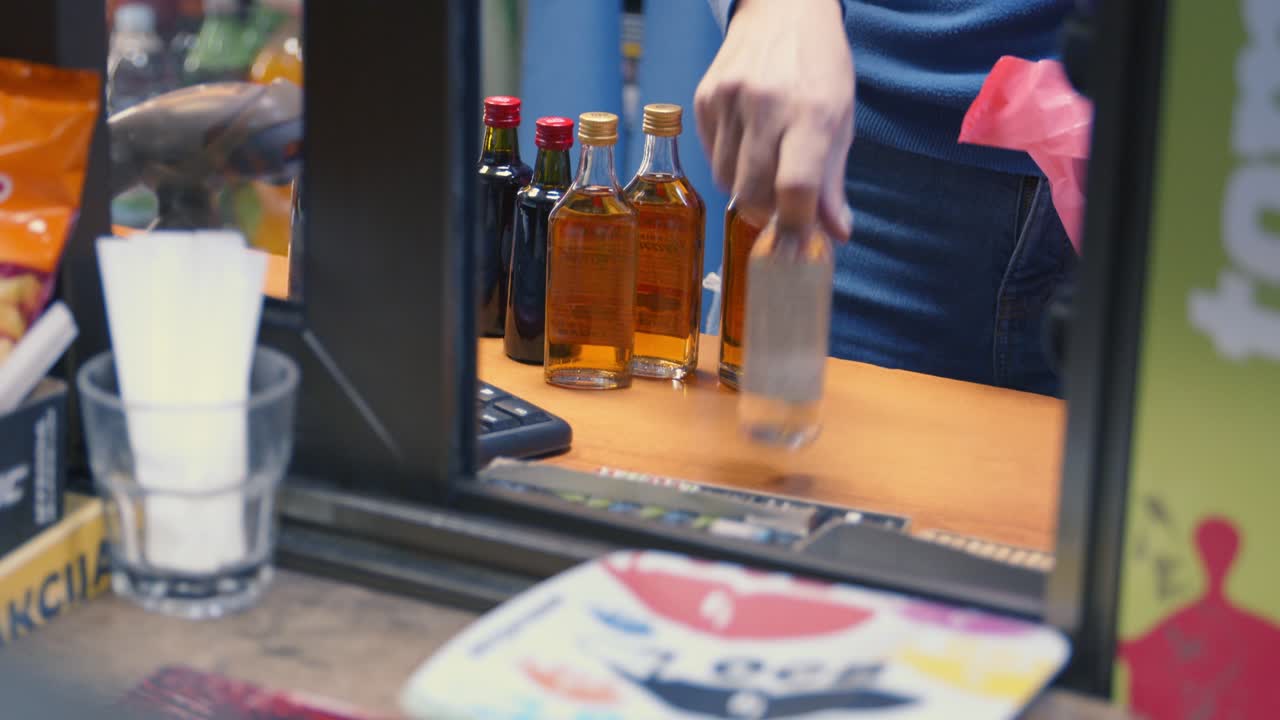 O vendedor coloca pequenas garrafas de bebidas alcoólicas em um saco plástico e o cliente paga com uma nota.