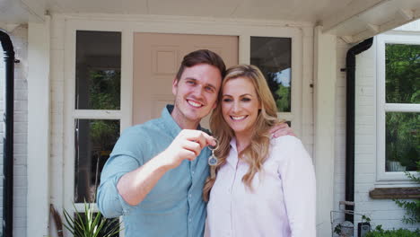 portrait of couple holding keys to new home standing outside front door