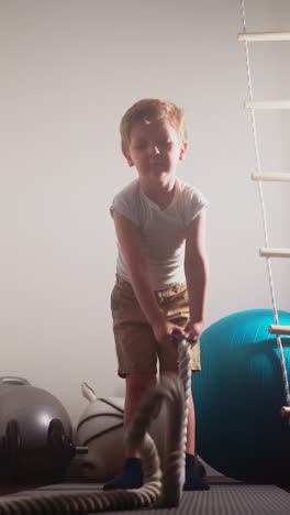 motivated toddler tries workout with battle rope in hands. strong little boy stands in gym using professional equipment for training slow motion