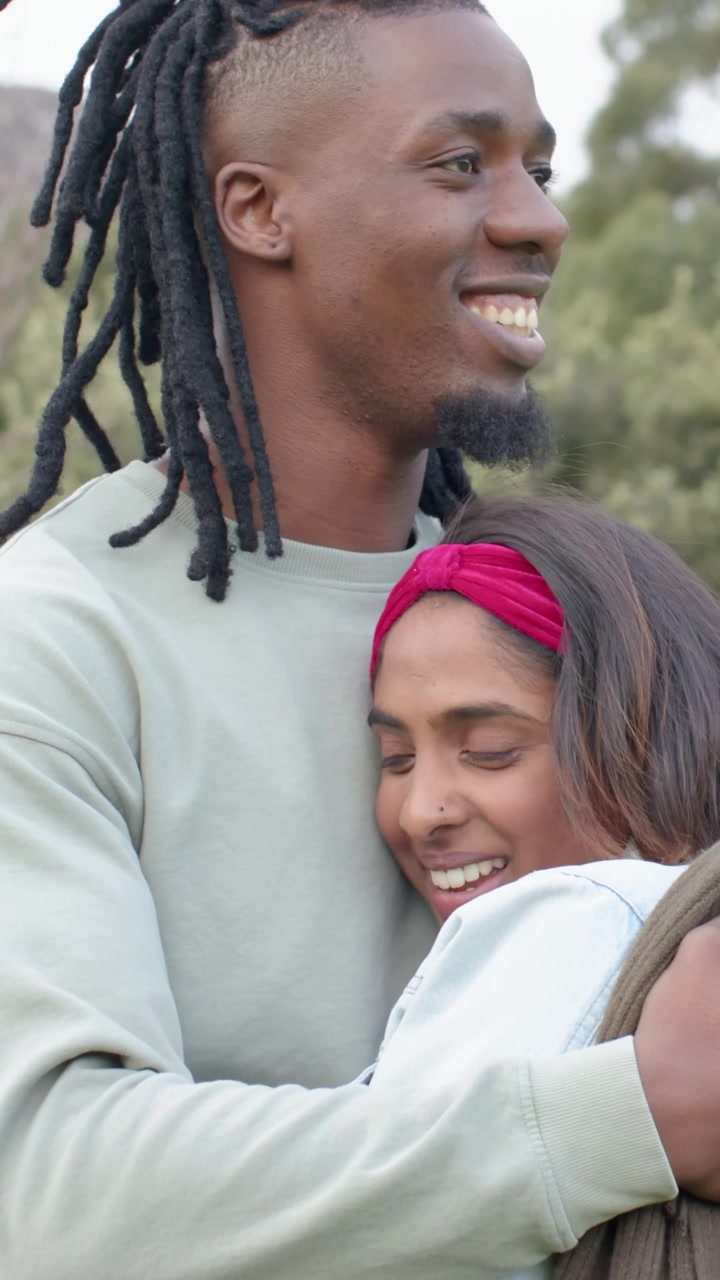 Vertical video: Close-up showing man in green top hugging woman in woods, holding mat for affection