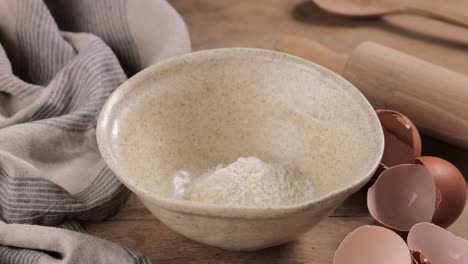 cook puts flour in a bowl with a wooden spoon for making dough