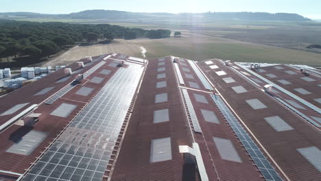 Aerial-drone-shot-flying-above-the-roof-of-a-remote-farm-building-covered-in-Solar-panels,-the-farm-investing-in-renewable-energy-for-sustainable-agriculture-which-is-green-and-echo-friendly