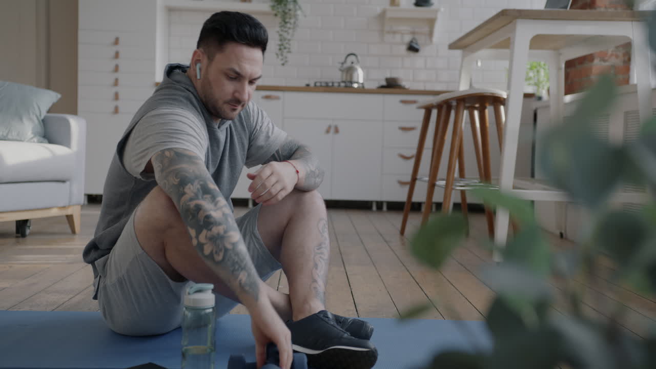 Man doing home workout with dumbbells and smartphone