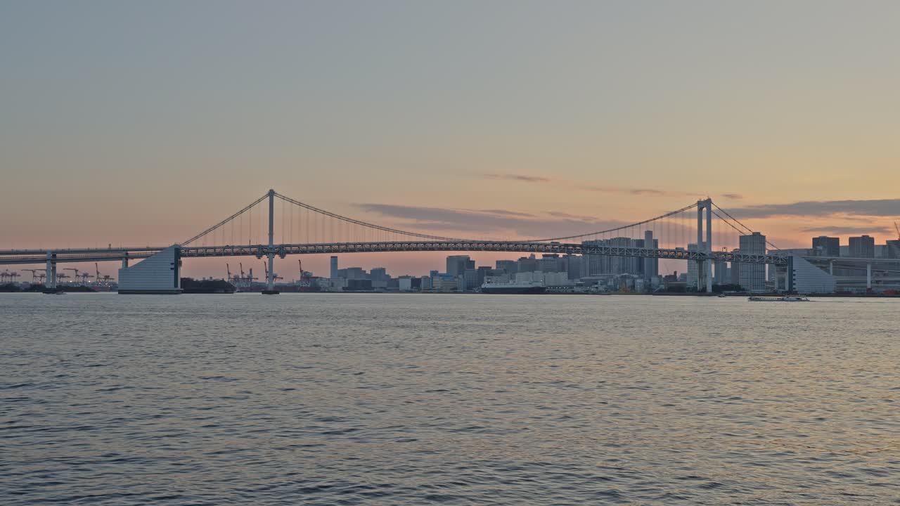 Low-angle shot of the Harumi Signal Station tower with the Tokyo Bay skyline and Rainbow Bridge visible at twilight