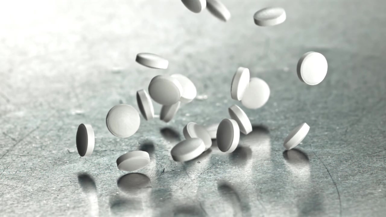 Pastillas blancas cayendo a cámara lenta sobre una superficie metálica