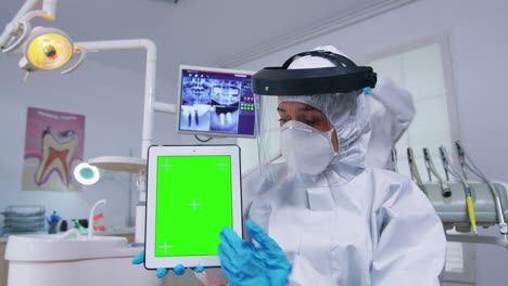 doctor in ppe suit showing tablet with green screen