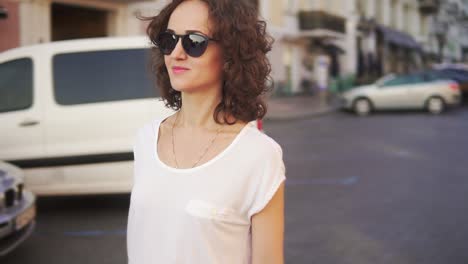 Happy-woman-in-sunglasses-walking-in-the-old-city-street-holding-her-stylish-longboard-in-the-morning.-Slow-motion-shot