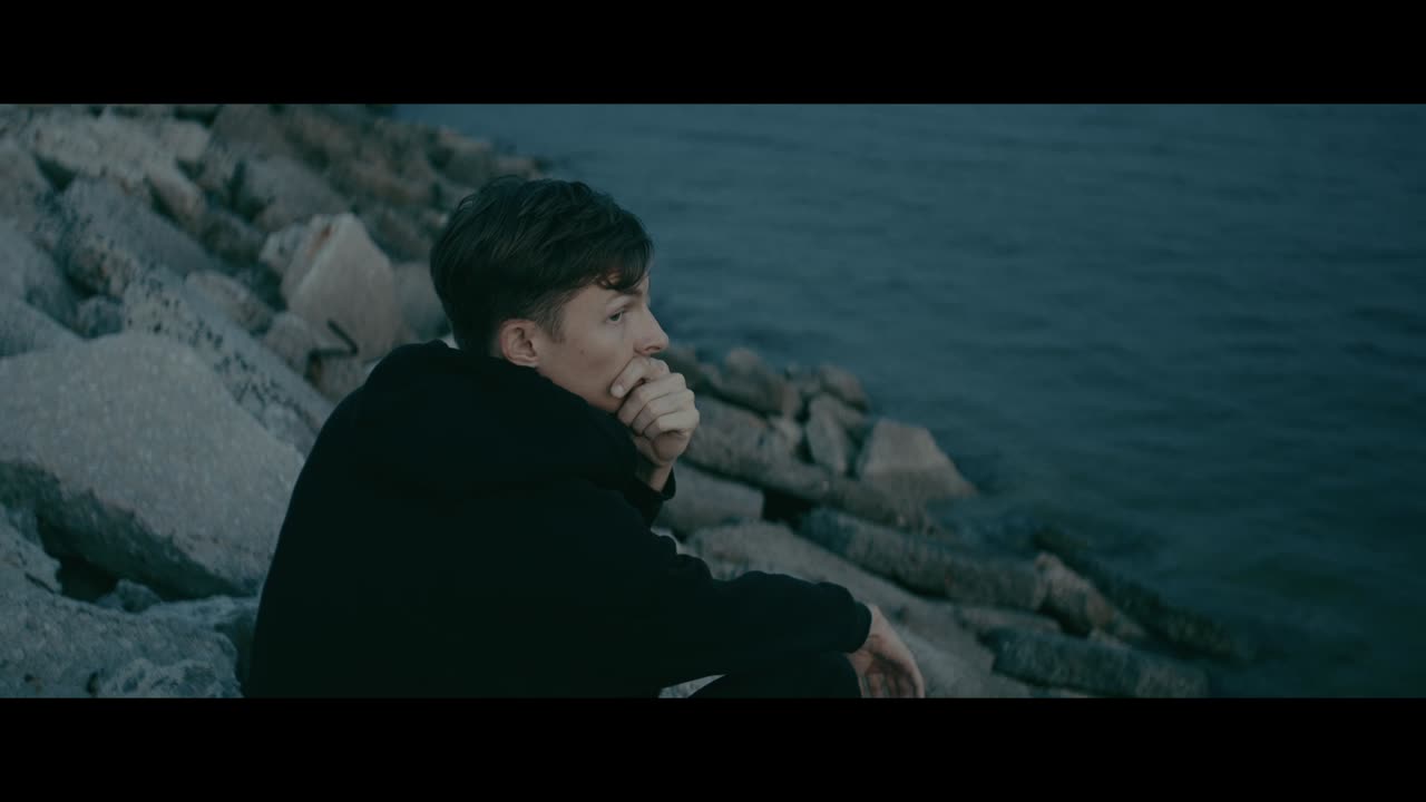 Man Sitting on Rocks by the Ocean