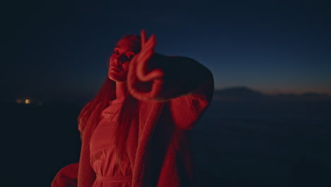 neon girl performer dancing on twilight seashore at evening. woman moving body