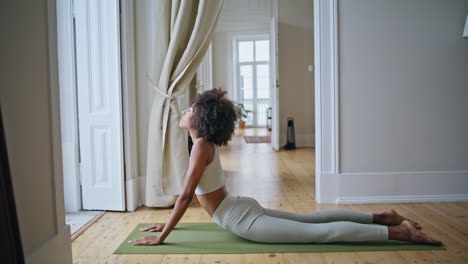 mujer fuerte cobra postura practicando en casa. chica africana estirando el cuerpo yoga asana
