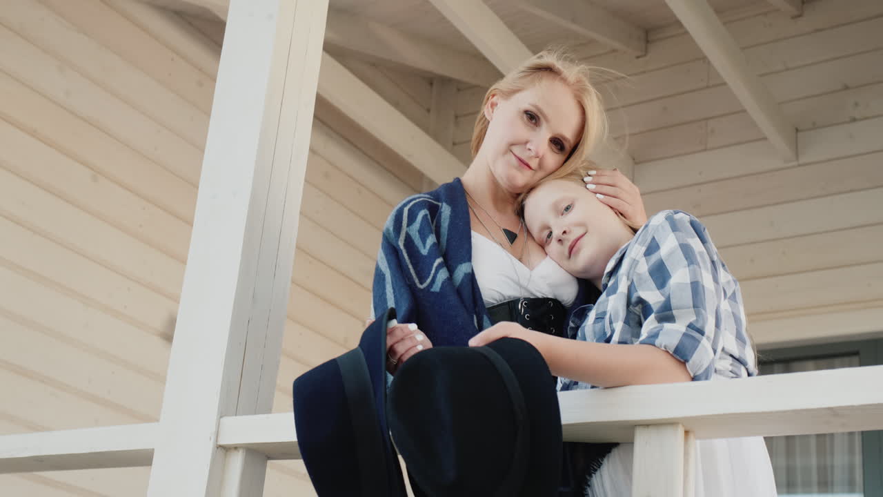 어머니와 딸이 손에 모자를 들고 목조 주택 현관에 서 있다 1