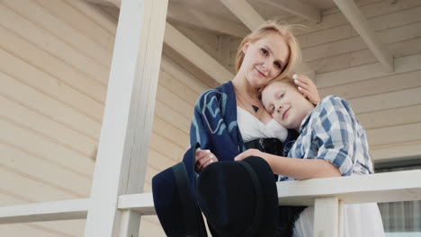 Mother-and-daughter-stand-on-the-porch-of-a-wooden-house-holding-hats-in-their-hands-1