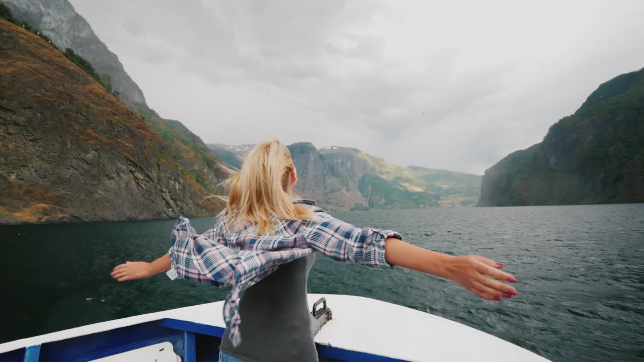 una mujer libre se para con las manos a los lados en la proa de un crucero que viaja por los fiordos de