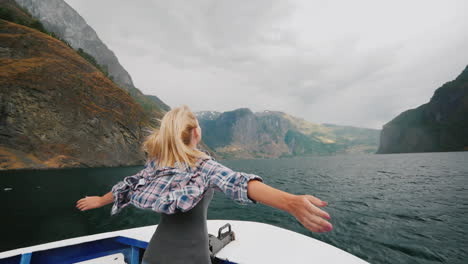 a free woman stands with her hands to the sides on the bow of a cruise ship traveling the fjords of