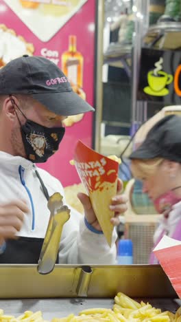man serving french fries at a street food stall
