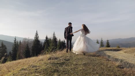 Recién-Casados.-Novio-Caucásico-Con-Novia-Corriendo-Por-La-Ladera-De-La-Montaña.-Pareja-De-Novios