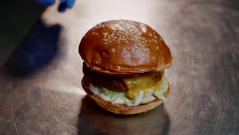 las manos del chef de comida rápida terminan de armar la hamburguesa de queso, primer plano