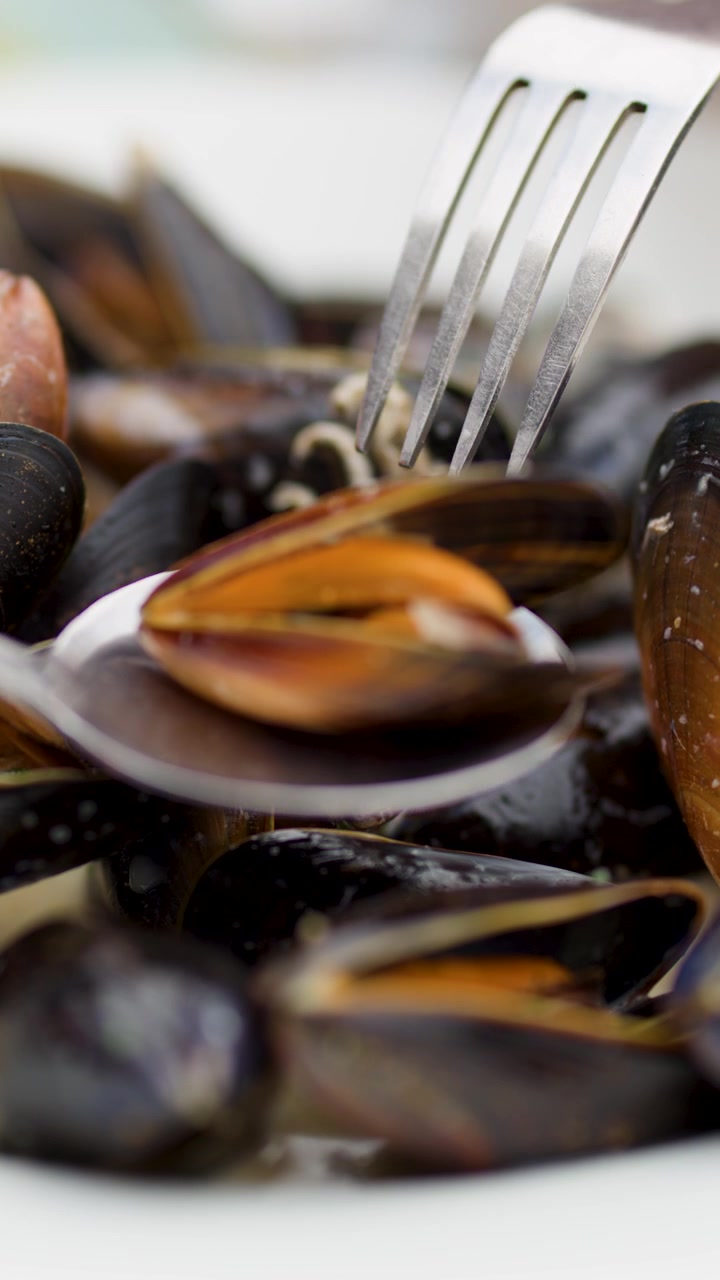 Close-up of utensils lifting mussels from a plate, natural lighting, shallow depth of field
