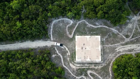 un avión no tripulado se eleva lentamente por encima de un camión y tres personas caminando en una plataforma de helicóptero en medio de un bosque tropical en las islas caimán en el caribe