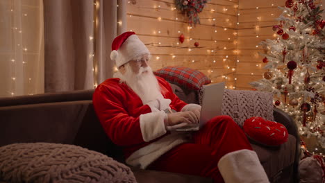 santa sits at home on a couch with a laptop and answers children's emails