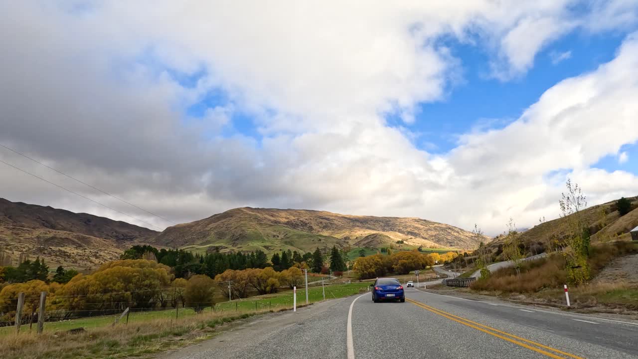 A serene drive through Wanaka, showcasing vibrant autumn foliage, rolling hills, and dynamic skies under changing light conditions