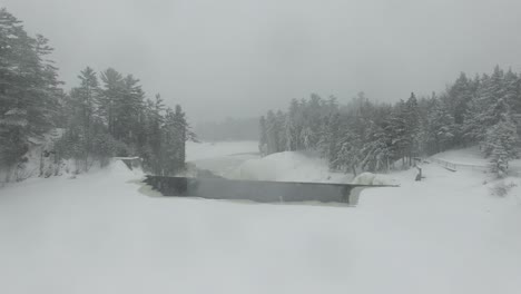 Drone-flying-over-frozen-river-while-approaching-edge-of-water-falling-into-lake