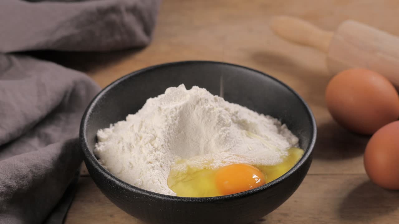 cook brakes an egg in a bowl of flour for making dough