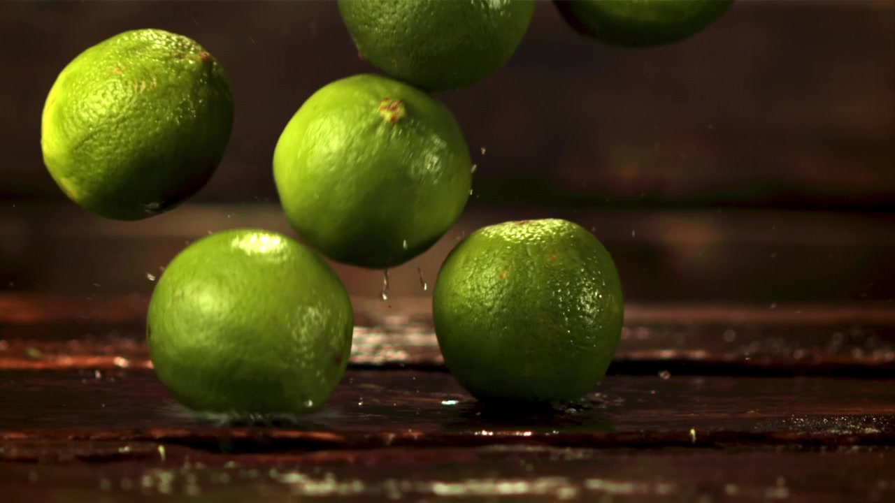 Lime freschi che cadono e schizzano acqua su una superficie di legno bagnata al rallentatore