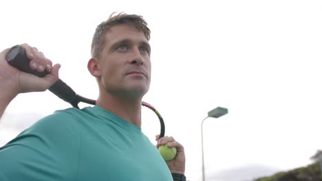 Serious-caucasian-male-tennis-player-holding-racket-and-ball-on-outdoor-court,-slow-motion
