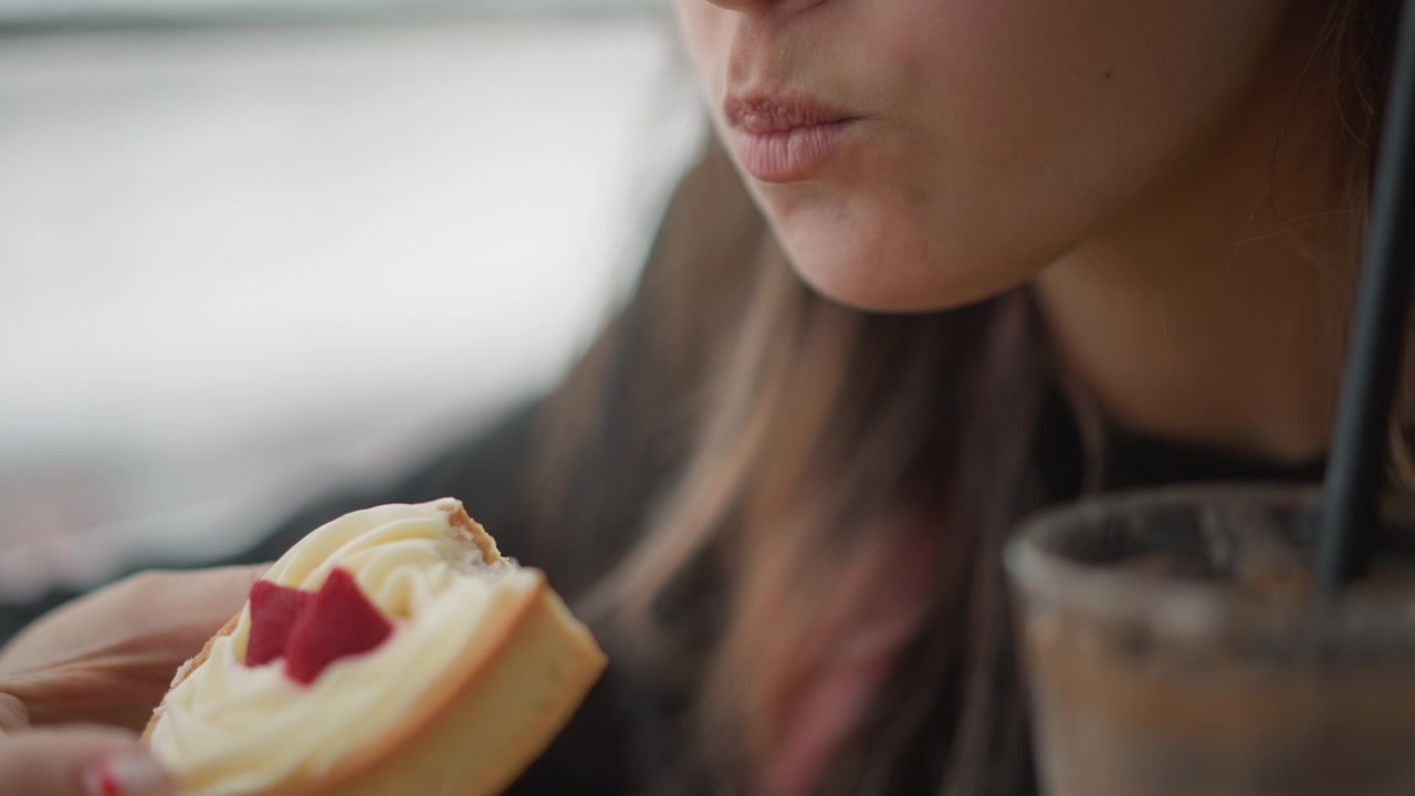 Close view shows young woman holding cream topped strawberry pastry near face, eyes closed and lips relaxed while savoring taste. Soft natural window light, calm indoor cafe setting, intimate mood