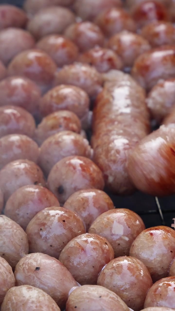 Close-up of sizzling sausage balls cooking over open flame, smoke rising, handheld camera movement