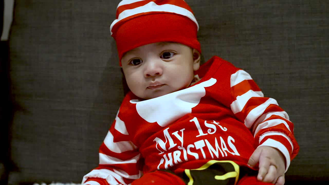 Entzückendes, süßes zwei Monate altes Baby im festlichen roten Weihnachtsoutfit auf der Couch