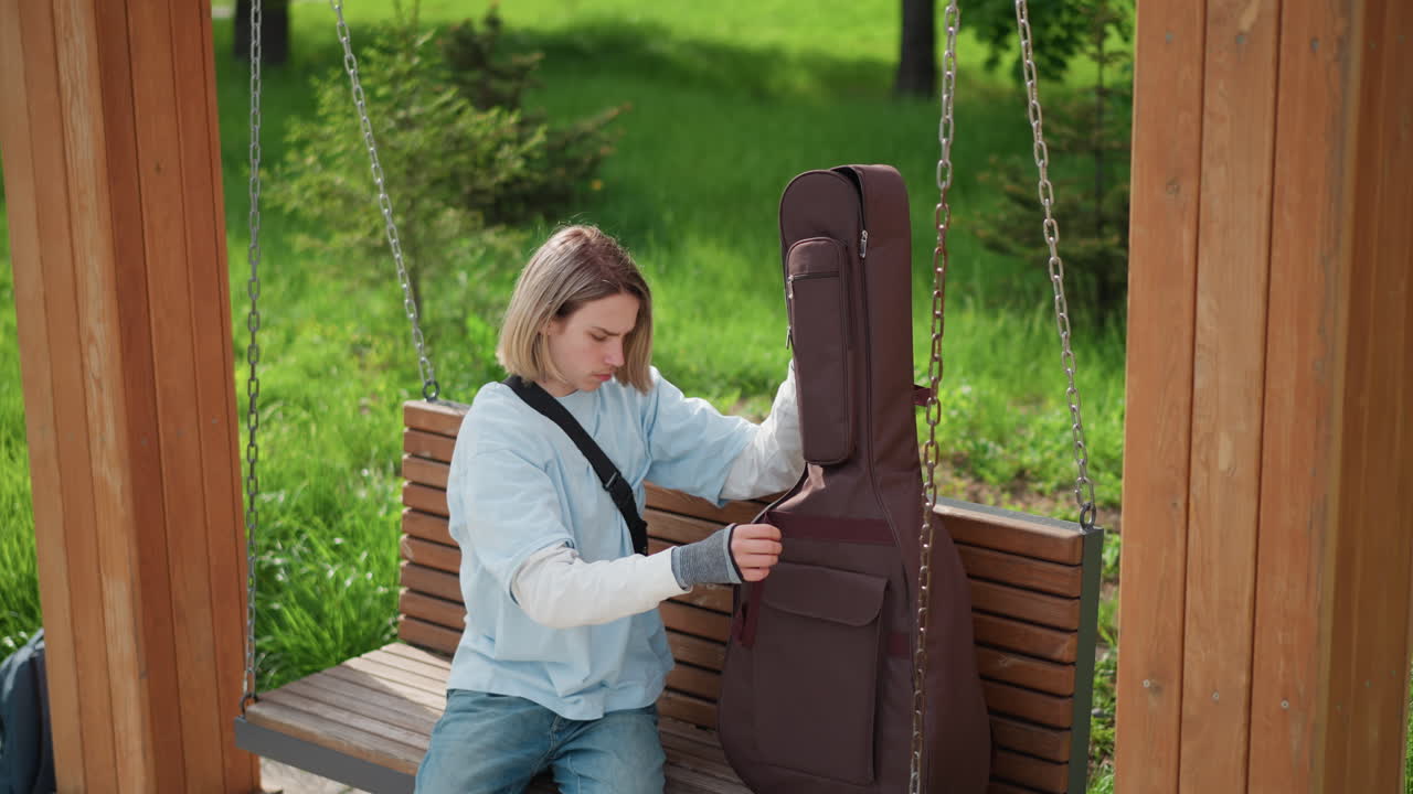 Un giovane artista accorda e modifica lo strumento. Un musicista pensieroso prepara silenziosamente la sua chitarra tra gli alberi. Un musicista calmo modifica il suo strumento con attenzione mentre è seduto su una panchina del parco vicino agli alberi.