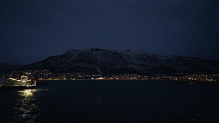 Montagne enneigée en face d'un port de la Norvège arctique avec des lumières côtières brillantes à l'heure bleue