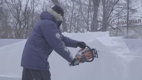 man carving a large snow sculpture with a chainsaw