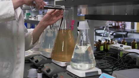 científico en bata de laboratorio mezclando productos químicos en una botella de vidrio en un laboratorio