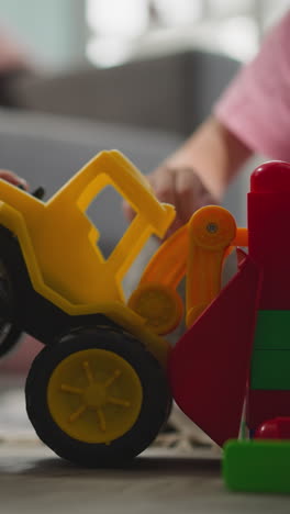 toddler tries to move wall built with small blocks by sister using bulldozer. little boy plays with vehicle toys on blurry background closeup